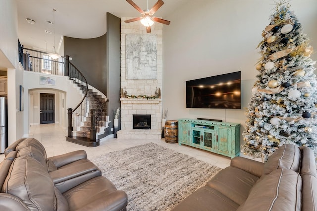 tiled living room featuring a fireplace, a towering ceiling, and ceiling fan