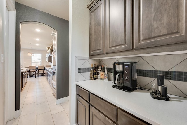 bar featuring arched walkways, light tile patterned floors, baseboards, and decorative backsplash