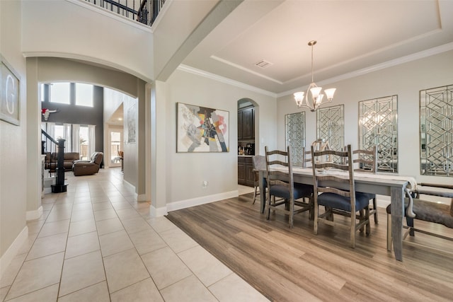 dining area with arched walkways, baseboards, light wood-style flooring, an inviting chandelier, and stairs