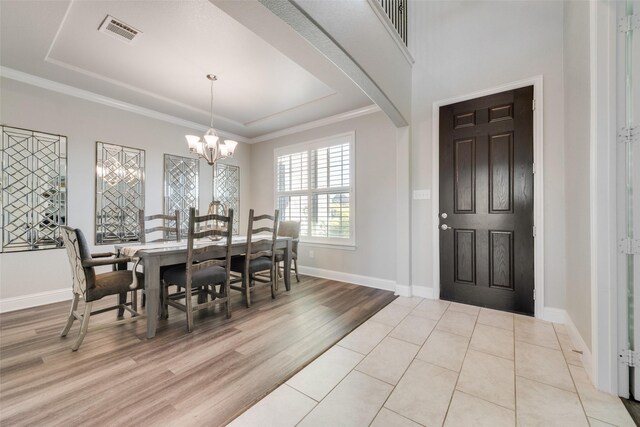 dining space with a raised ceiling, light wood-type flooring, an inviting chandelier, and crown molding