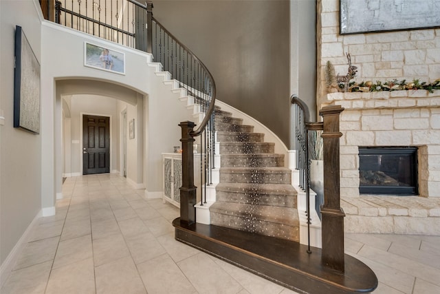 interior space with arched walkways, a fireplace, a towering ceiling, baseboards, and stairs