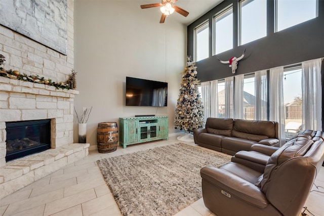 living room with ceiling fan, light tile patterned floors, a fireplace, and a high ceiling