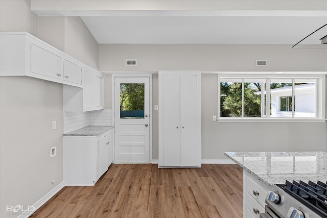 kitchen featuring gas stove, light stone countertops, light hardwood / wood-style flooring, and white cabinets