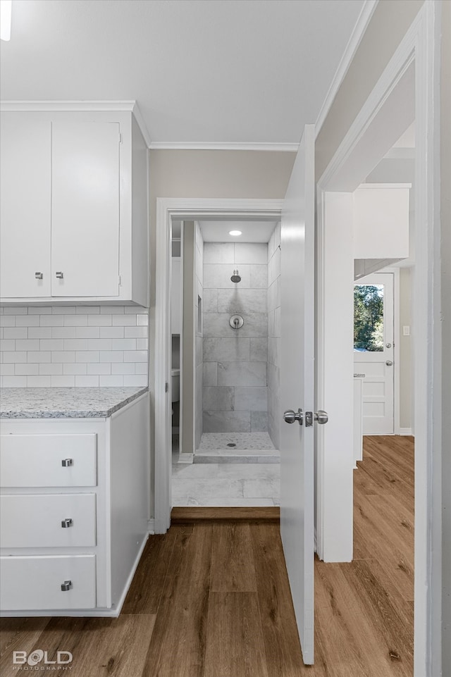 bathroom with crown molding, hardwood / wood-style flooring, tiled shower, and backsplash