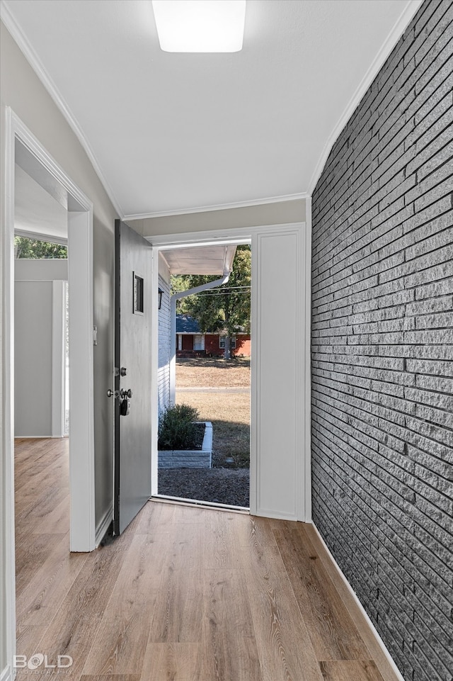 foyer entrance featuring light hardwood / wood-style flooring, ornamental molding, and brick wall