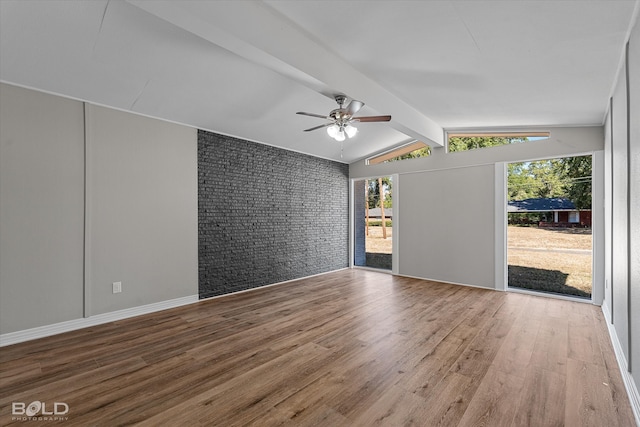 empty room featuring vaulted ceiling with beams, hardwood / wood-style flooring, brick wall, and ceiling fan