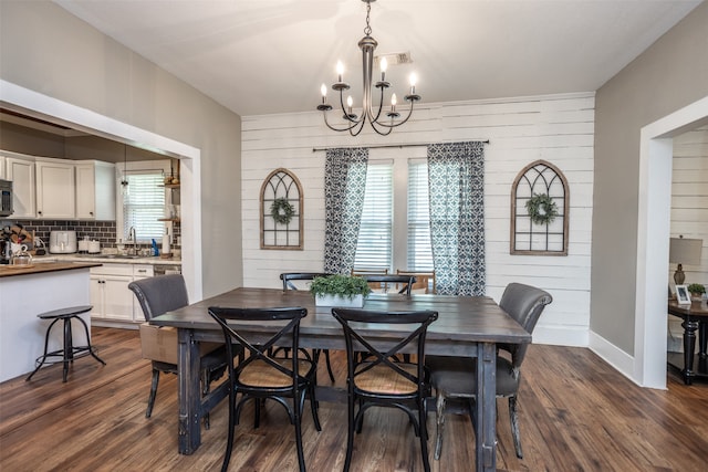 dining area with a notable chandelier, wood walls, sink, and dark hardwood / wood-style flooring