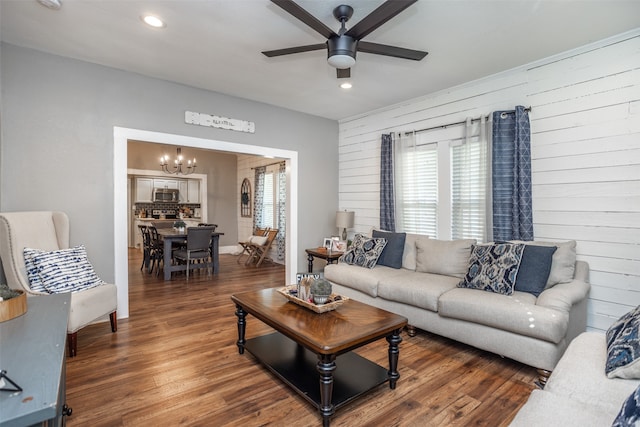 living room with wooden walls, ceiling fan with notable chandelier, and dark hardwood / wood-style flooring