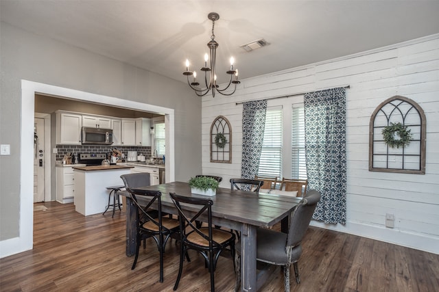 dining space featuring sink, dark hardwood / wood-style flooring, wooden walls, and an inviting chandelier