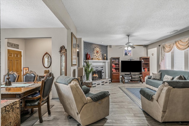 living room with a fireplace, light hardwood / wood-style floors, a textured ceiling, and ceiling fan