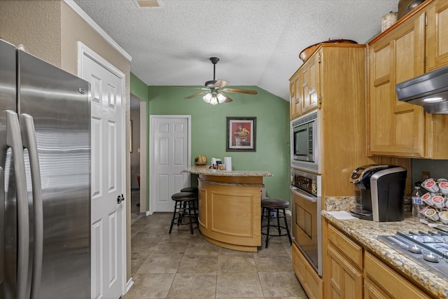 kitchen featuring a textured ceiling, appliances with stainless steel finishes, lofted ceiling, a kitchen breakfast bar, and light stone counters