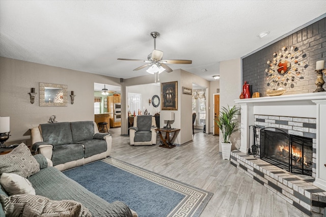 living room with ceiling fan, a brick fireplace, light hardwood / wood-style flooring, and a textured ceiling