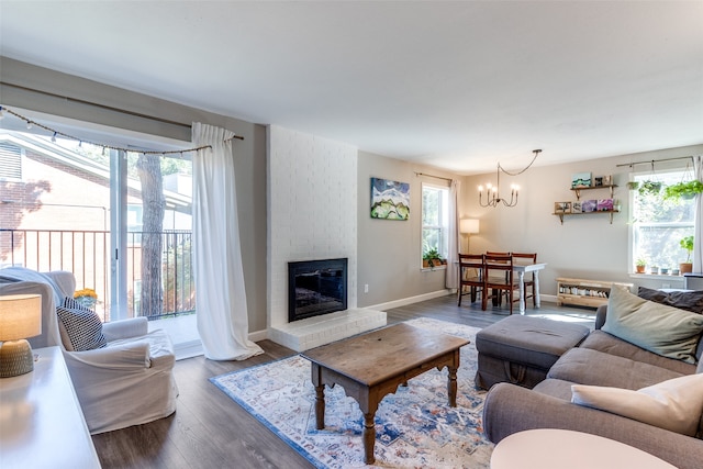 living room with an inviting chandelier, dark wood-type flooring, a fireplace, and a wealth of natural light