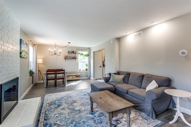 living room featuring a brick fireplace, hardwood / wood-style flooring, and an inviting chandelier