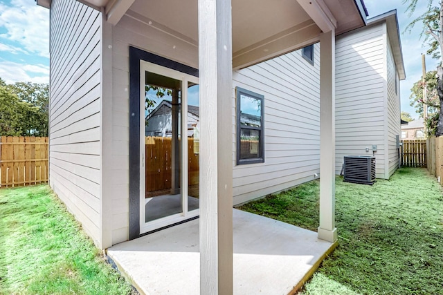 view of exterior entry with a patio, cooling unit, and a yard