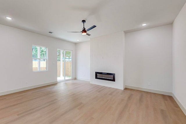 unfurnished living room featuring a large fireplace, light hardwood / wood-style flooring, and ceiling fan