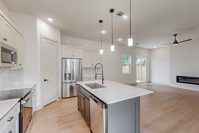 kitchen featuring appliances with stainless steel finishes, sink, white cabinetry, pendant lighting, and a kitchen island with sink