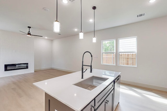 kitchen featuring an island with sink, hanging light fixtures, light hardwood / wood-style flooring, sink, and stainless steel dishwasher