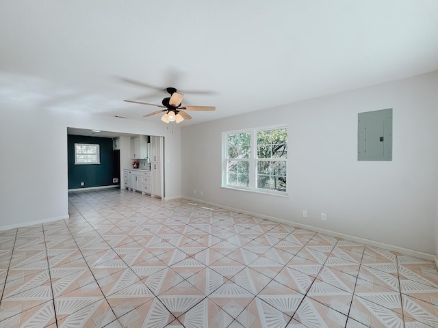 empty room featuring ceiling fan, a wealth of natural light, light tile patterned floors, and electric panel