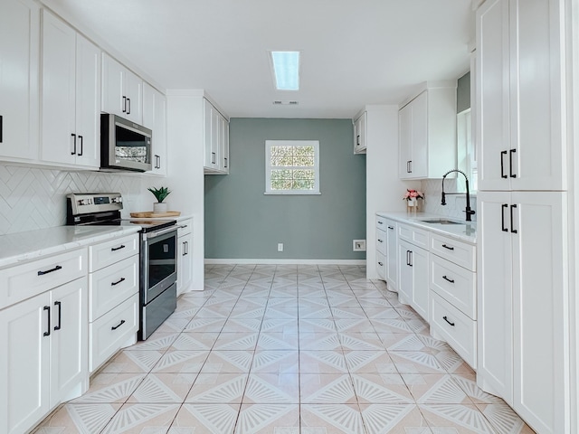 kitchen with tasteful backsplash, a skylight, stainless steel appliances, sink, and white cabinets