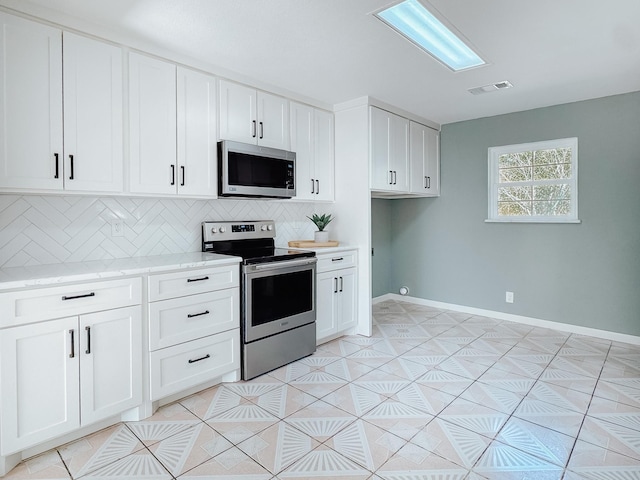 kitchen with light stone countertops, backsplash, stainless steel appliances, light tile patterned floors, and white cabinetry