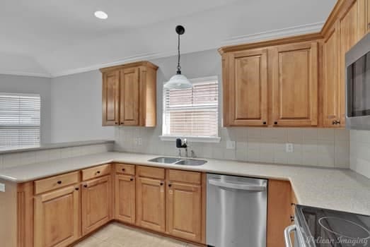 kitchen with appliances with stainless steel finishes, sink, decorative backsplash, hanging light fixtures, and ornamental molding