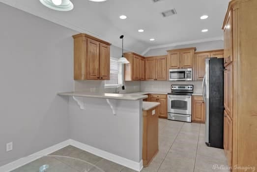 kitchen with a kitchen breakfast bar, hanging light fixtures, kitchen peninsula, stainless steel appliances, and light tile patterned floors