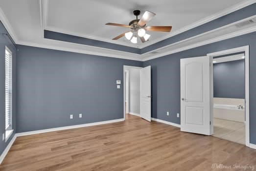 unfurnished bedroom featuring a raised ceiling, crown molding, light wood-type flooring, and ceiling fan