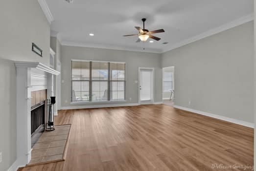 unfurnished living room featuring light hardwood / wood-style floors, crown molding, a tile fireplace, and ceiling fan