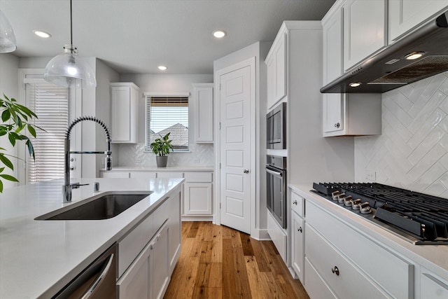 kitchen featuring under cabinet range hood, appliances with stainless steel finishes, light countertops, and a sink