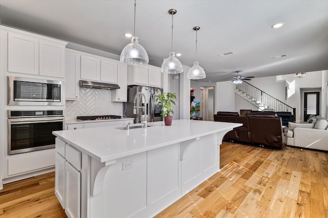 kitchen with sink, white cabinets, hanging light fixtures, a kitchen island with sink, and stainless steel appliances