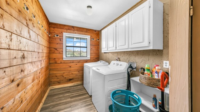 clothes washing area with cabinets, wooden walls, washing machine and clothes dryer, and dark hardwood / wood-style flooring