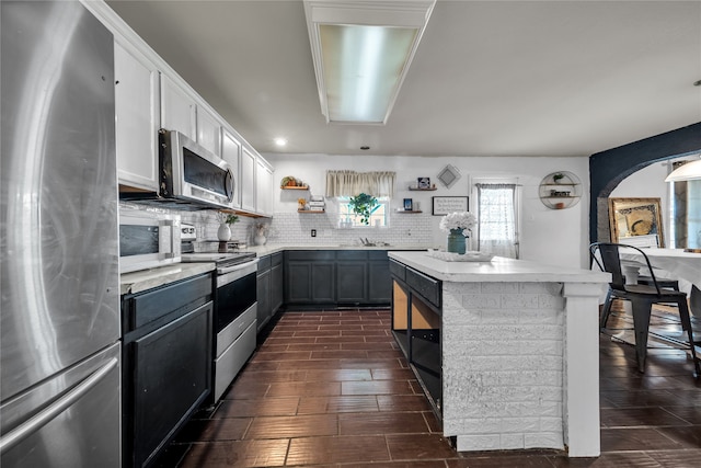 kitchen with a kitchen island, decorative backsplash, white cabinets, appliances with stainless steel finishes, and dark hardwood / wood-style flooring