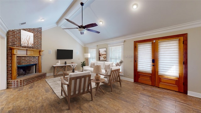 living room with lofted ceiling with beams, a brick fireplace, hardwood / wood-style floors, ceiling fan, and crown molding