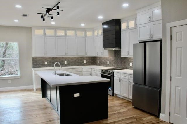 kitchen with appliances with stainless steel finishes, sink, custom exhaust hood, white cabinets, and a center island with sink