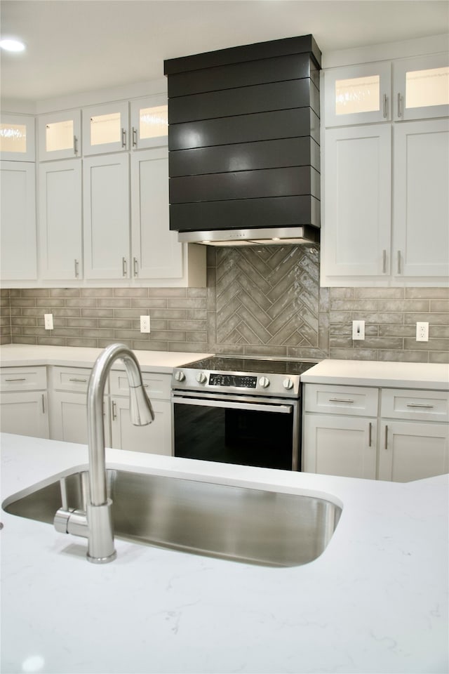 kitchen with decorative backsplash, white cabinetry, stainless steel range with electric cooktop, and premium range hood