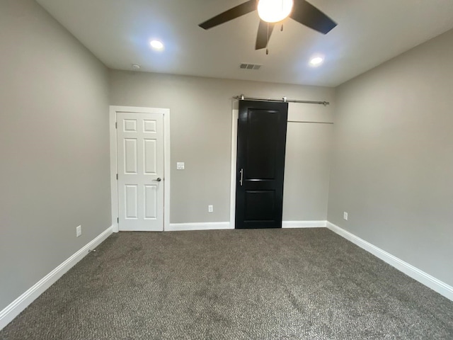 unfurnished bedroom with a barn door, dark colored carpet, and ceiling fan