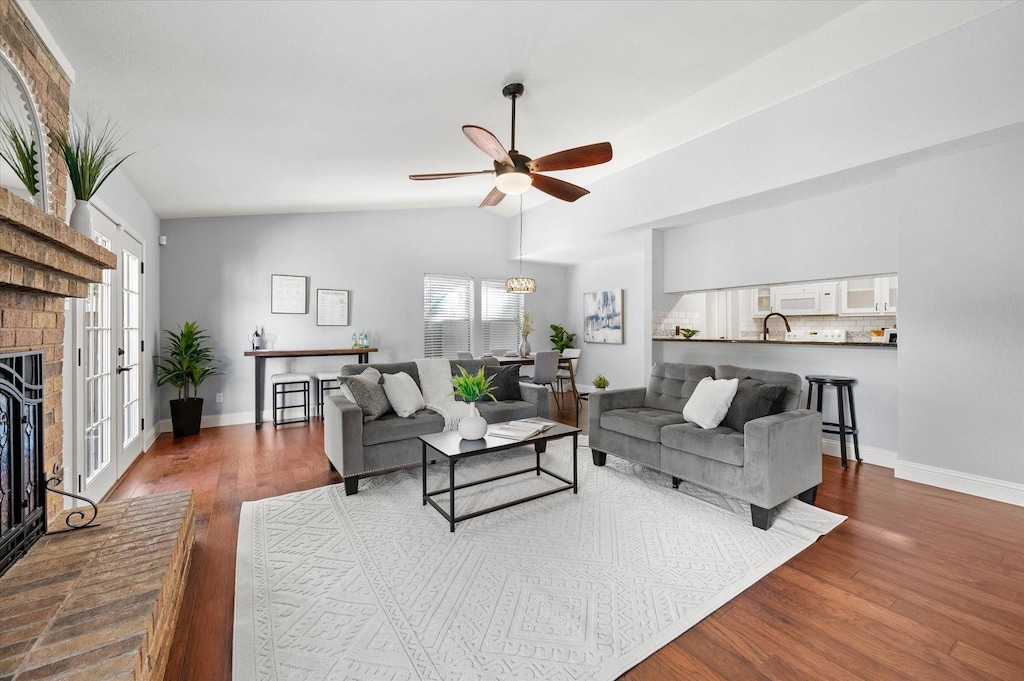 living room featuring vaulted ceiling, ceiling fan, dark hardwood / wood-style floors, and a brick fireplace