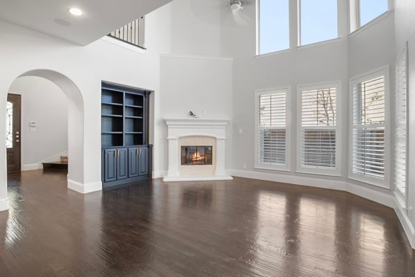 unfurnished living room with dark wood-type flooring, ceiling fan, built in features, and a towering ceiling