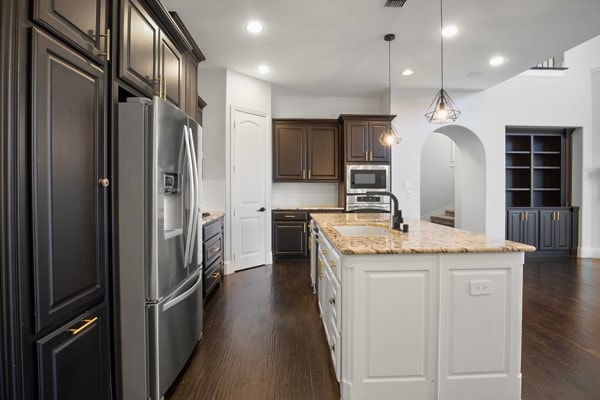 kitchen featuring sink, an island with sink, stainless steel appliances, decorative light fixtures, and dark hardwood / wood-style floors