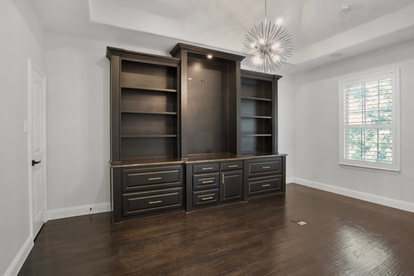 unfurnished living room featuring a raised ceiling, an inviting chandelier, and dark hardwood / wood-style floors