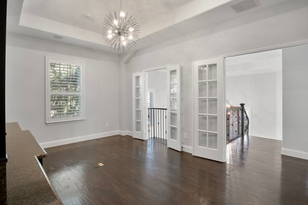 spare room with dark wood-type flooring, french doors, a tray ceiling, and a chandelier