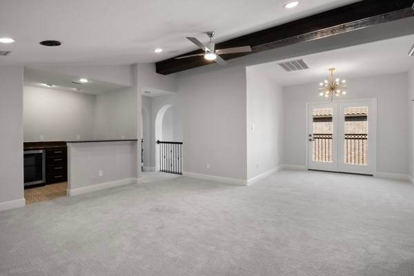 carpeted empty room featuring beamed ceiling, beverage cooler, and ceiling fan with notable chandelier