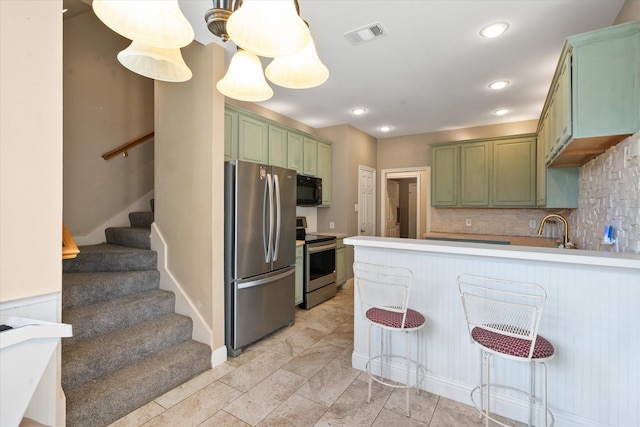 kitchen with backsplash, green cabinets, kitchen peninsula, stainless steel appliances, and a breakfast bar