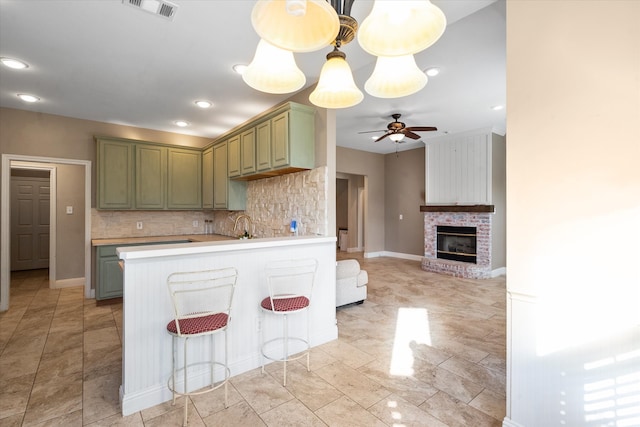 kitchen with decorative backsplash, kitchen peninsula, green cabinetry, a fireplace, and ceiling fan