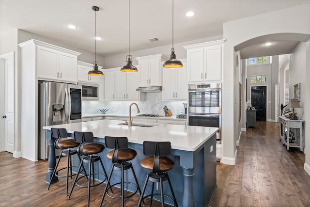 kitchen with sink, pendant lighting, white cabinets, dark wood-type flooring, and a center island with sink