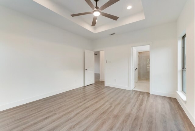 unfurnished bedroom featuring ceiling fan, a tray ceiling, light wood-type flooring, and ensuite bath