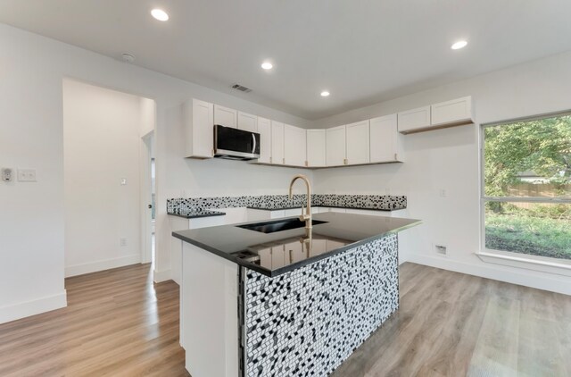 kitchen with a center island with sink, sink, white cabinetry, and light hardwood / wood-style floors