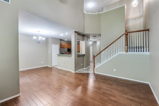 unfurnished living room featuring a towering ceiling, light hardwood / wood-style flooring, and a chandelier