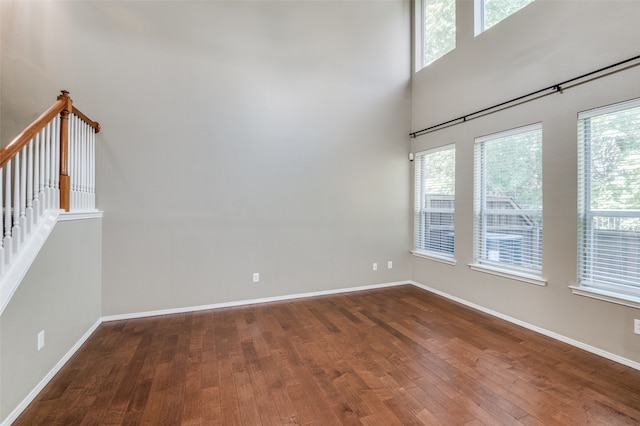 empty room featuring dark wood-type flooring, a high ceiling, and a wealth of natural light